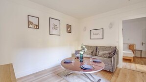 Un salon moderne avec une table ronde dressée pour le repas, un canapé gris et un lit dans la pièce adjacente.