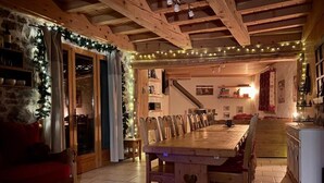 A cozy dining area with a long wooden table and chairs, a stone wall, and a staircase leading upstairs. - Ecrins Lodge (Le Bourg-d'Oisans)