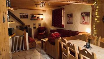 A cozy cabin interior with a wooden dining table, benches, a sofa, and a staircase.