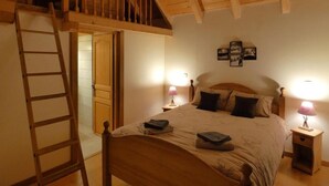 A bedroom with a loft-style bed, wooden beams, a ladder, two bedside lamps, and a framed picture on the wall. - Ecrins Lodge (Le Bourg-d'Oisans)