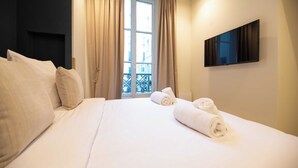 A hotel room with a large bed, beige curtains, a TV mounted on the wall, and a view of the outside balcony.