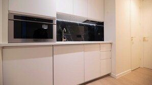 A modern kitchen with white cabinets, a built-in microwave, and a marble backsplash.