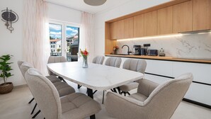 A modern kitchen with wooden cabinets, a marble countertop, and a dining area with a white table and grey chairs.