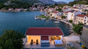 A coastal town with houses along the water, a dock with boats, and a building with a red roof and outdoor seating.