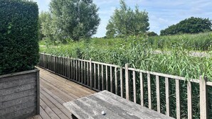 A wooden deck with a bench and a fence overlooking a grassy area with trees.