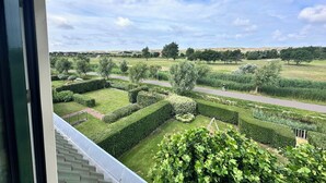 A view from a window overlooking a well-maintained garden with neatly trimmed hedges and a variety of trees.
