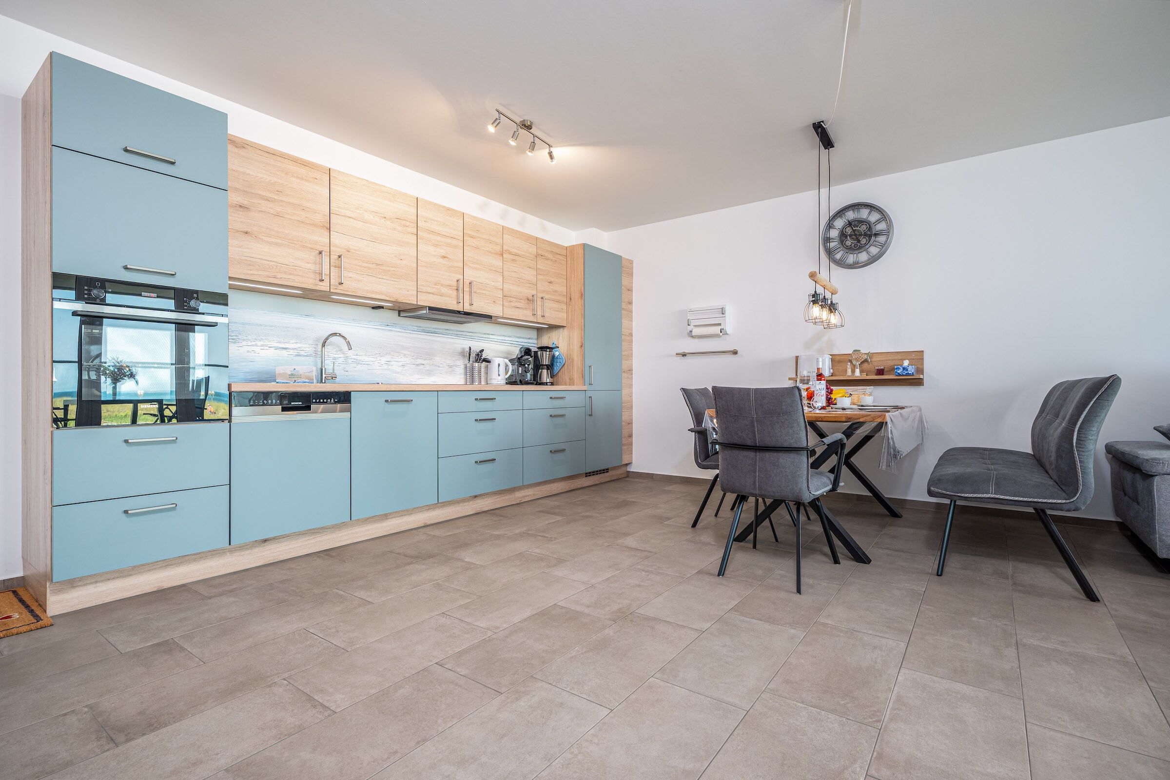 A modern kitchen with light blue cabinets, a stainless steel oven, and a dining area with two chairs and a table.