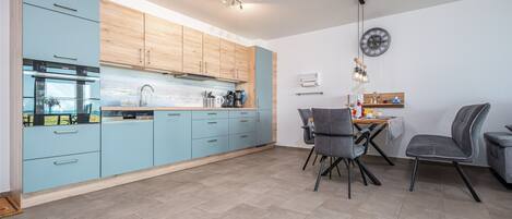 A modern kitchen with light blue cabinets, a stainless steel oven, and a dining area with two chairs and a table.