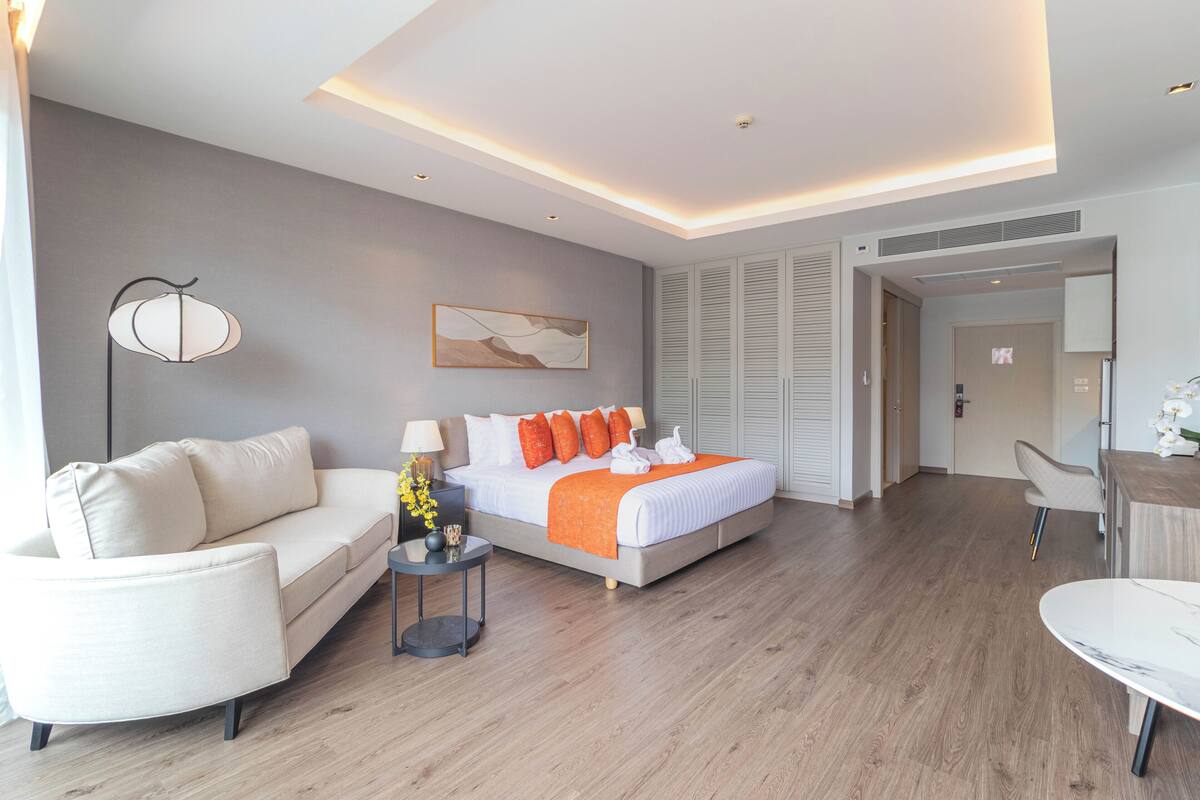 A modern hotel room with a bed, a sofa, a side table, and a desk.