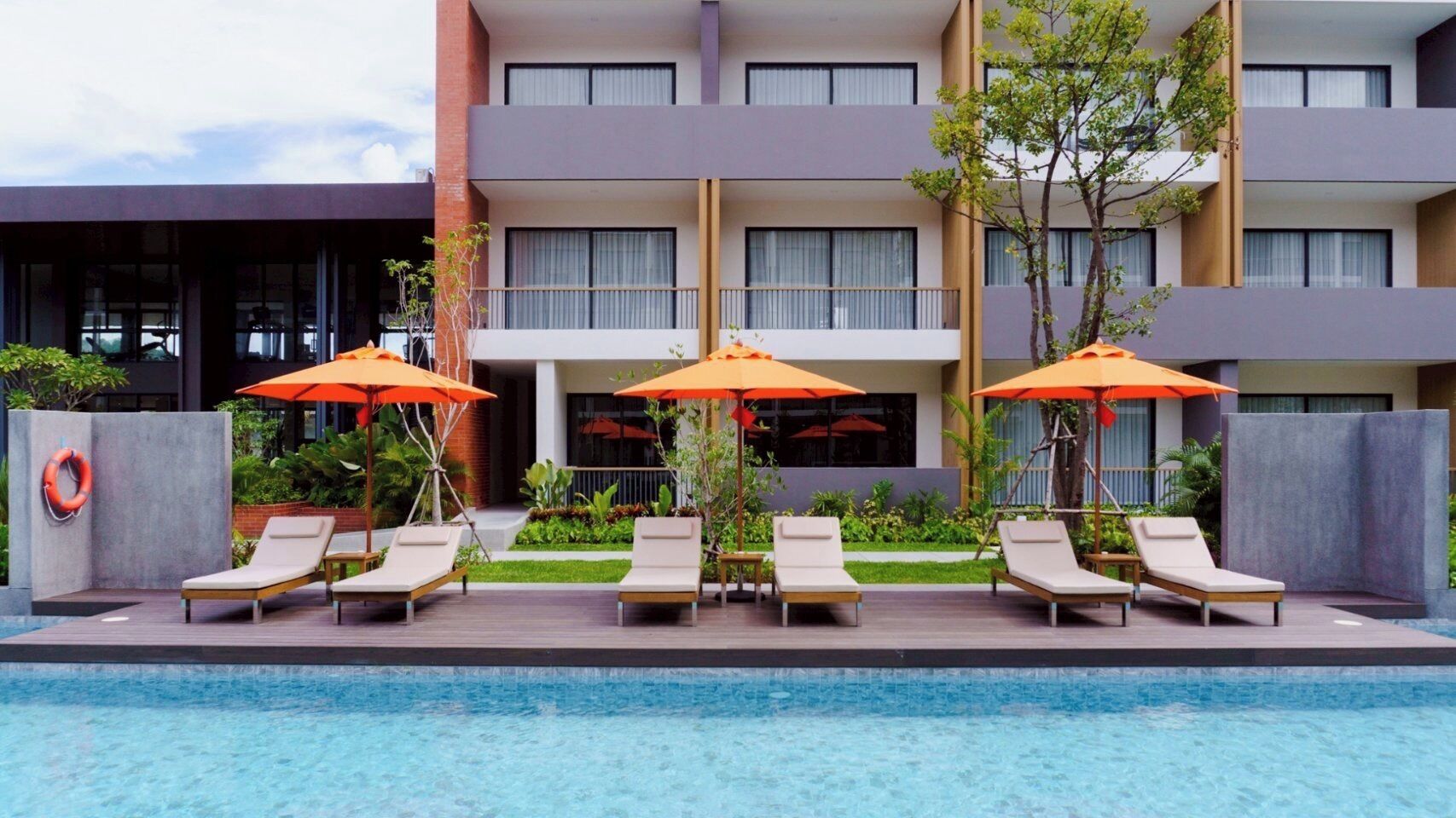 A modern hotel with a swimming pool, sun loungers, and orange umbrellas.
