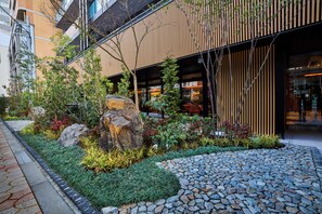 A modern building with a stone pathway, a variety of plants, and a large rock centerpiece. - ANCHORED by RIHGA OSAKA NAMBA (Osaka)