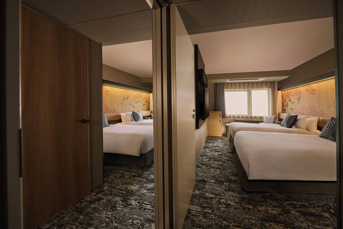 A hotel room with two beds, a large mirror, a TV, and a carpeted floor.
