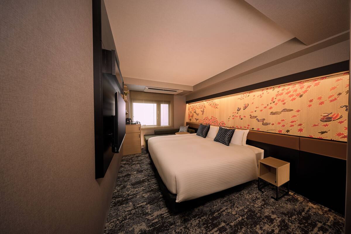 A hotel room with a large bed, a TV, a desk, and a window.