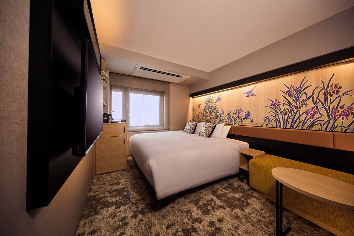 A hotel room with a bed, a TV, a small table, and a decorative wall.