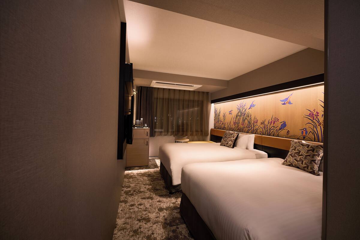 A hotel room with two beds, a desk, and a large window with curtains.