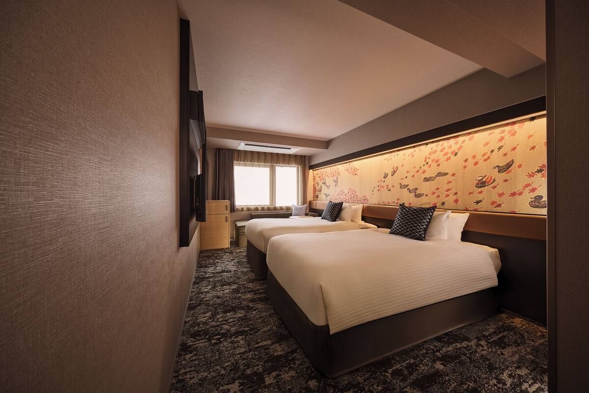 A hotel room with two beds, a large window, a wall-mounted TV, and a carpeted floor.