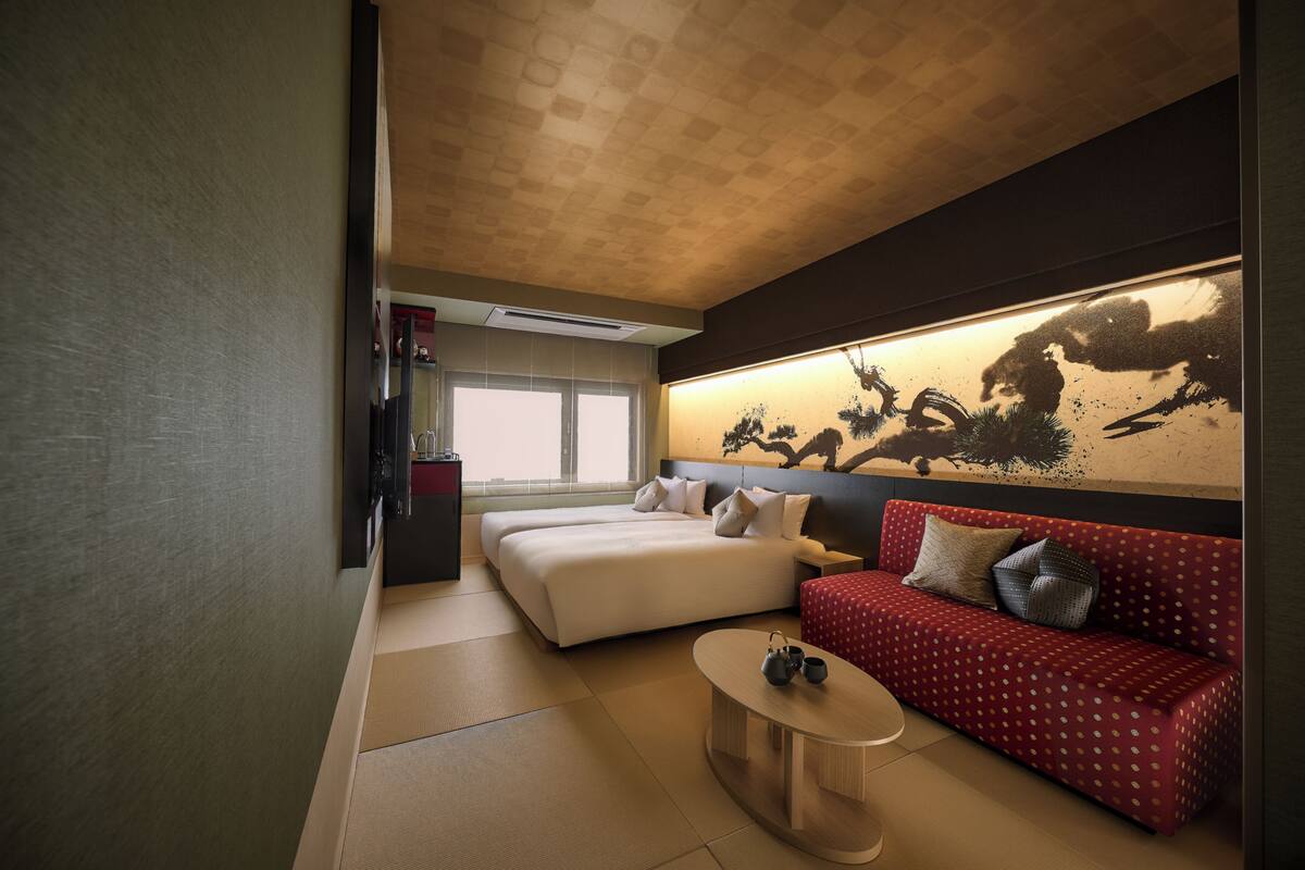 A hotel room with a bed, a sofa, a coffee table, and a large painting on the wall.