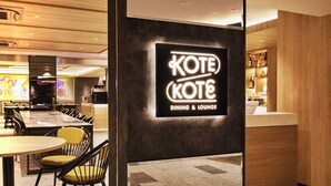 Una zona de menjador moderna amb un cartell de neó per a 'Kote Kote Dining & Lounge', que inclou una barra i diferents disposicions de seients.