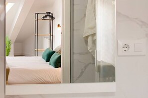 A bedroom with a bed, a green plant, a black metal rack, and a shower area.