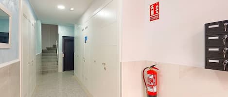A hallway with lockers, a fire extinguisher, and an exit sign.