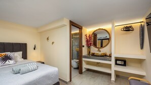 A modern bedroom with a bed, bedside table, and a bathroom with a vanity, mirror, and towel rack. - Symi's Jewel (Simi)