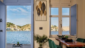 A dining area with a view of the sea, a wooden table, green chairs, and a potted plant. - Symi's Jewel (Simi)