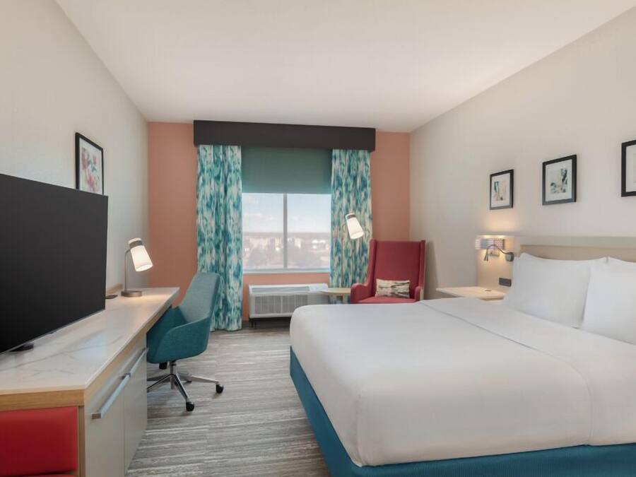 A hotel room with a bed, desk, chair, TV, and artwork on the walls.