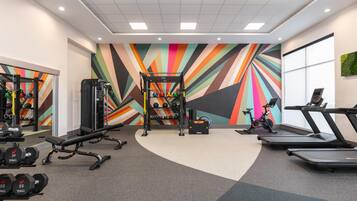 A gym with exercise equipment, treadmills, and a colorful wall design.