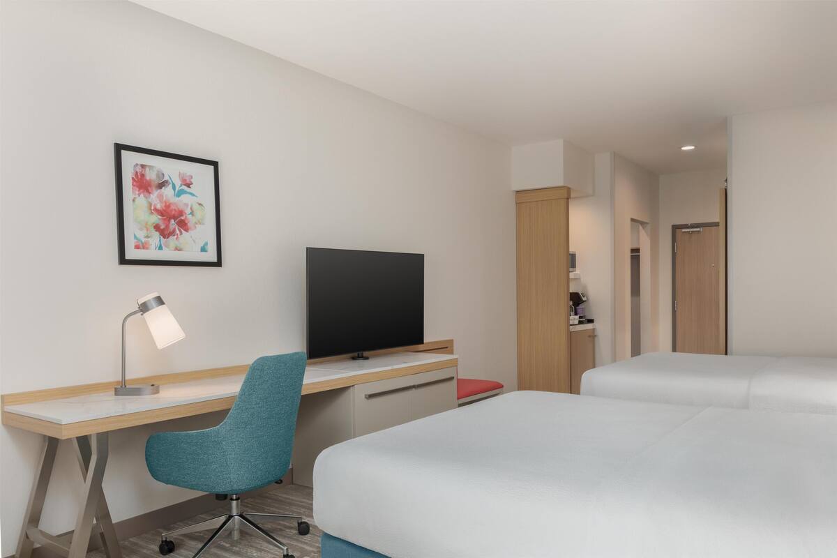 A hotel room with a desk, a TV, a chair, and two beds.
