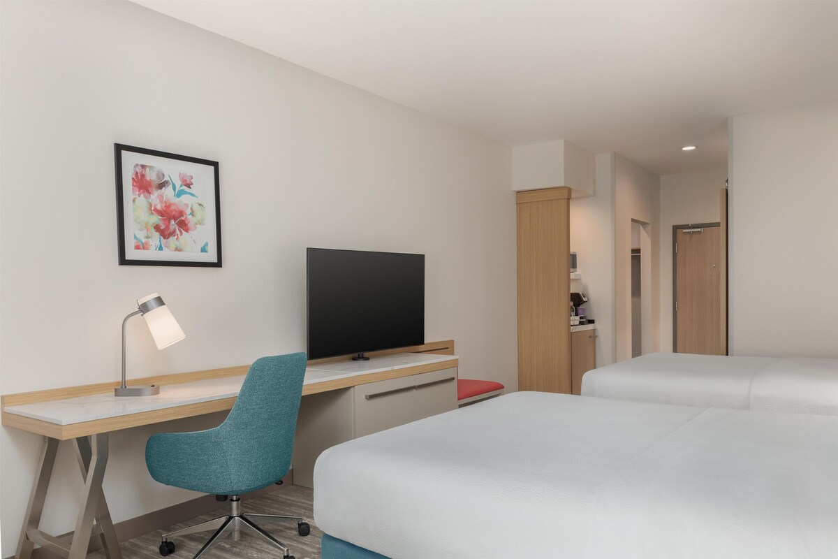 Une chambre d’hôtel équipée d’un bureau, d’une chaise, d’une télévision et de deux lits.