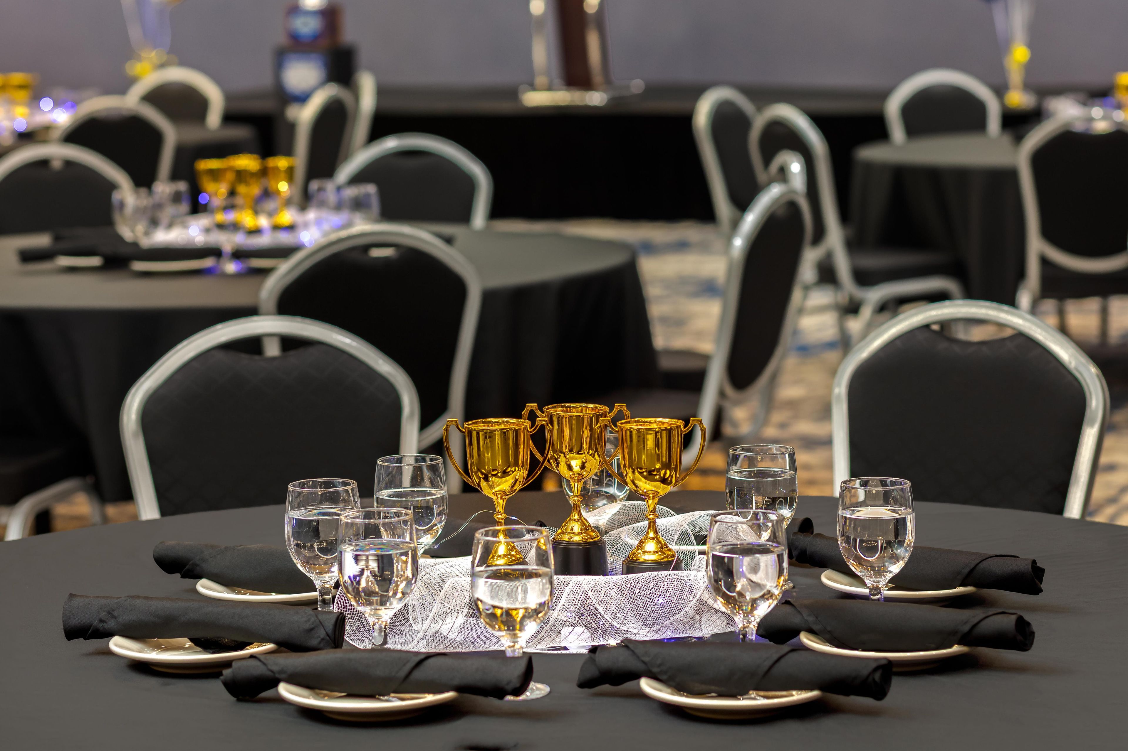 A banquet table set with glasses, plates, and golden trophies.
