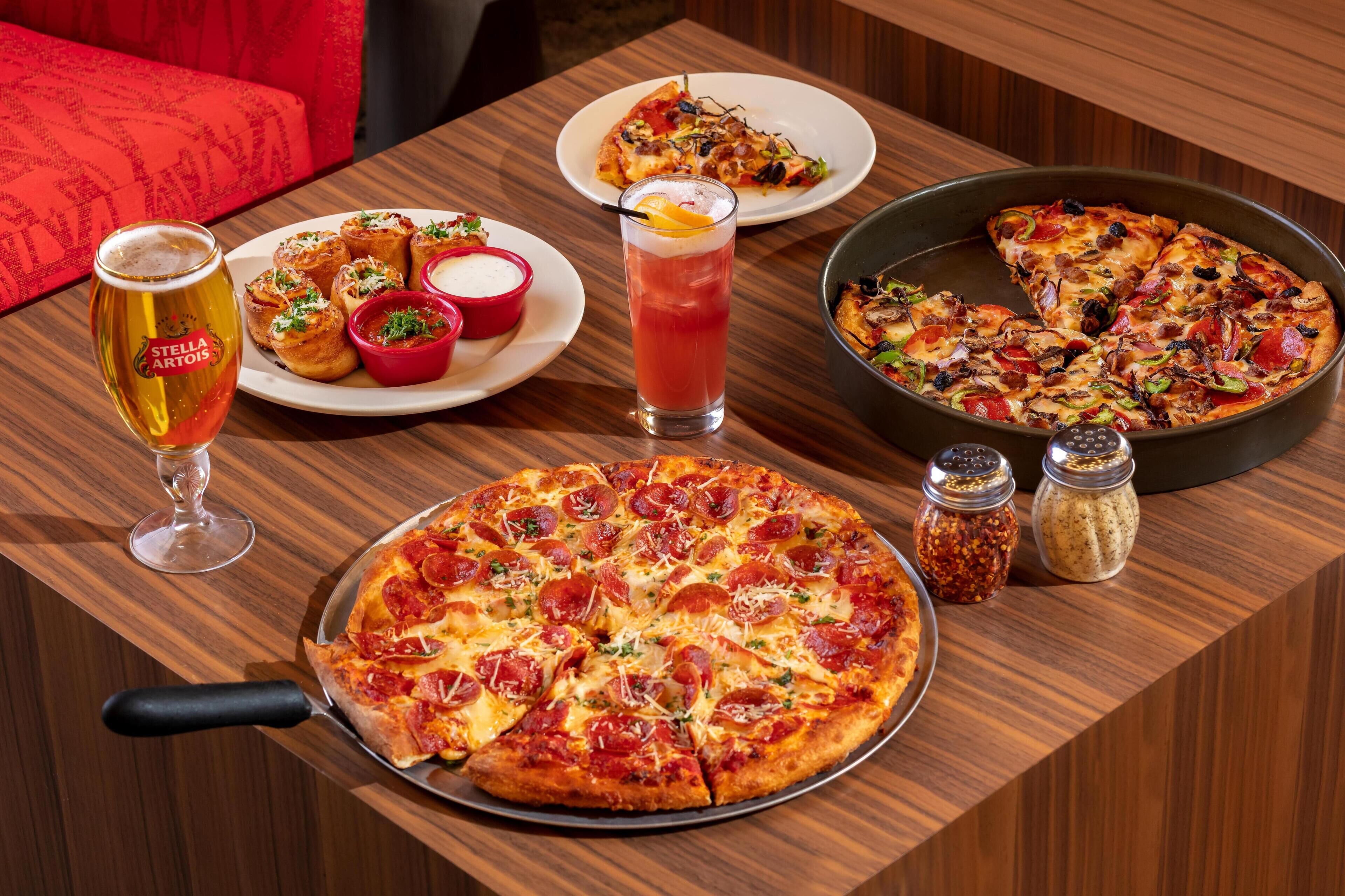 Pizza con pepperoni, una jarra de cerveza y dos platos de comida sobre una mesa de madera.