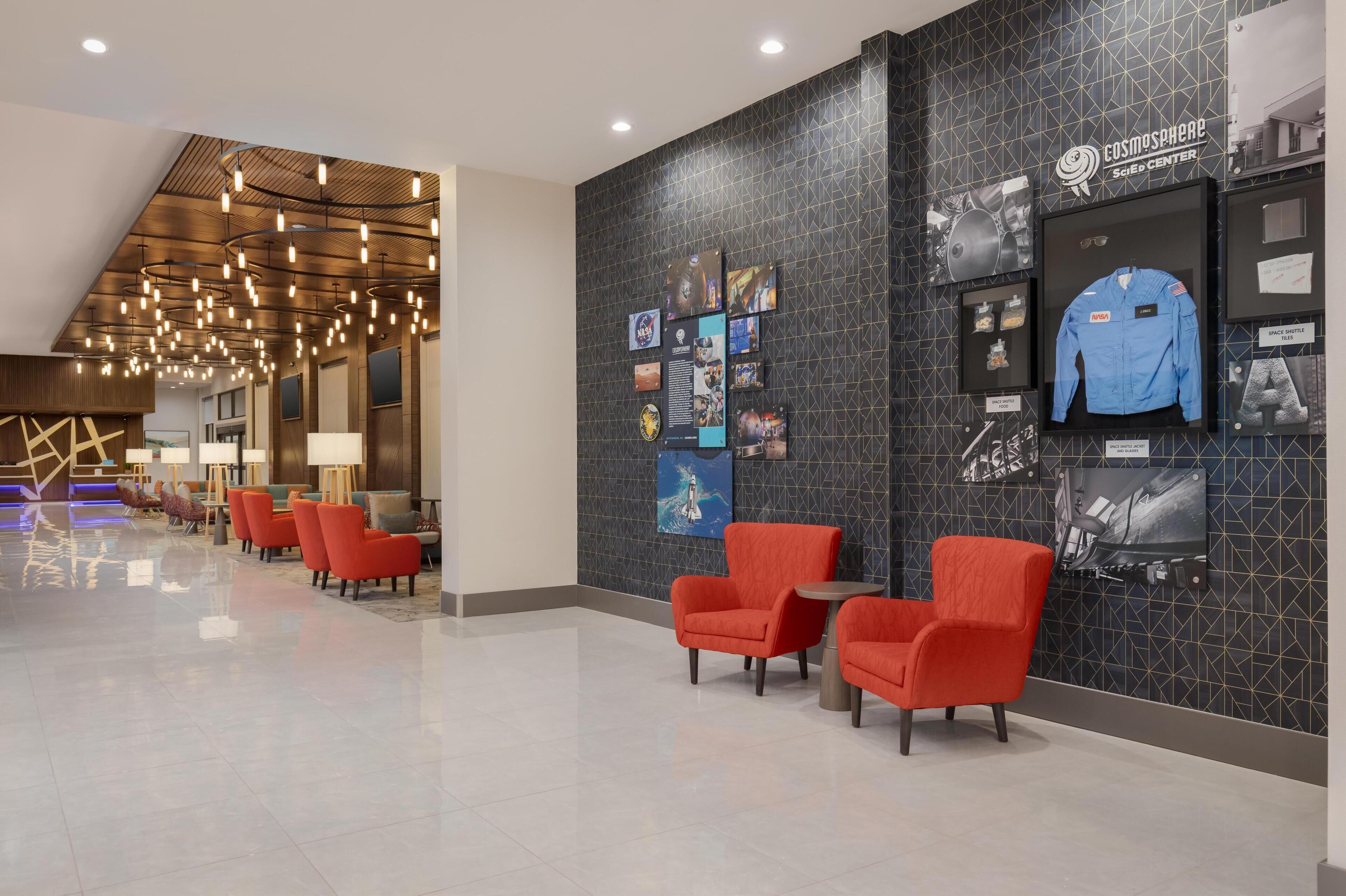 A modern hotel lobby with a geometric patterned wall, red chairs, and a Sci-Fi Center sign.