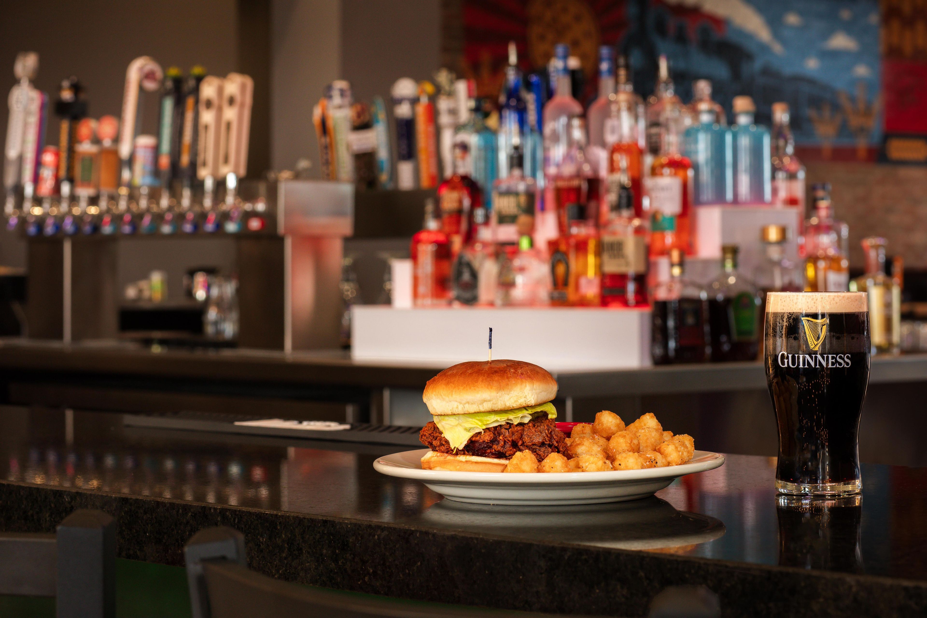 A bar setting with a burger, tater tots, and a Guinness beer glass.