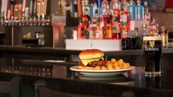 A bar setting with a burger, tater tots, and a Guinness beer glass.