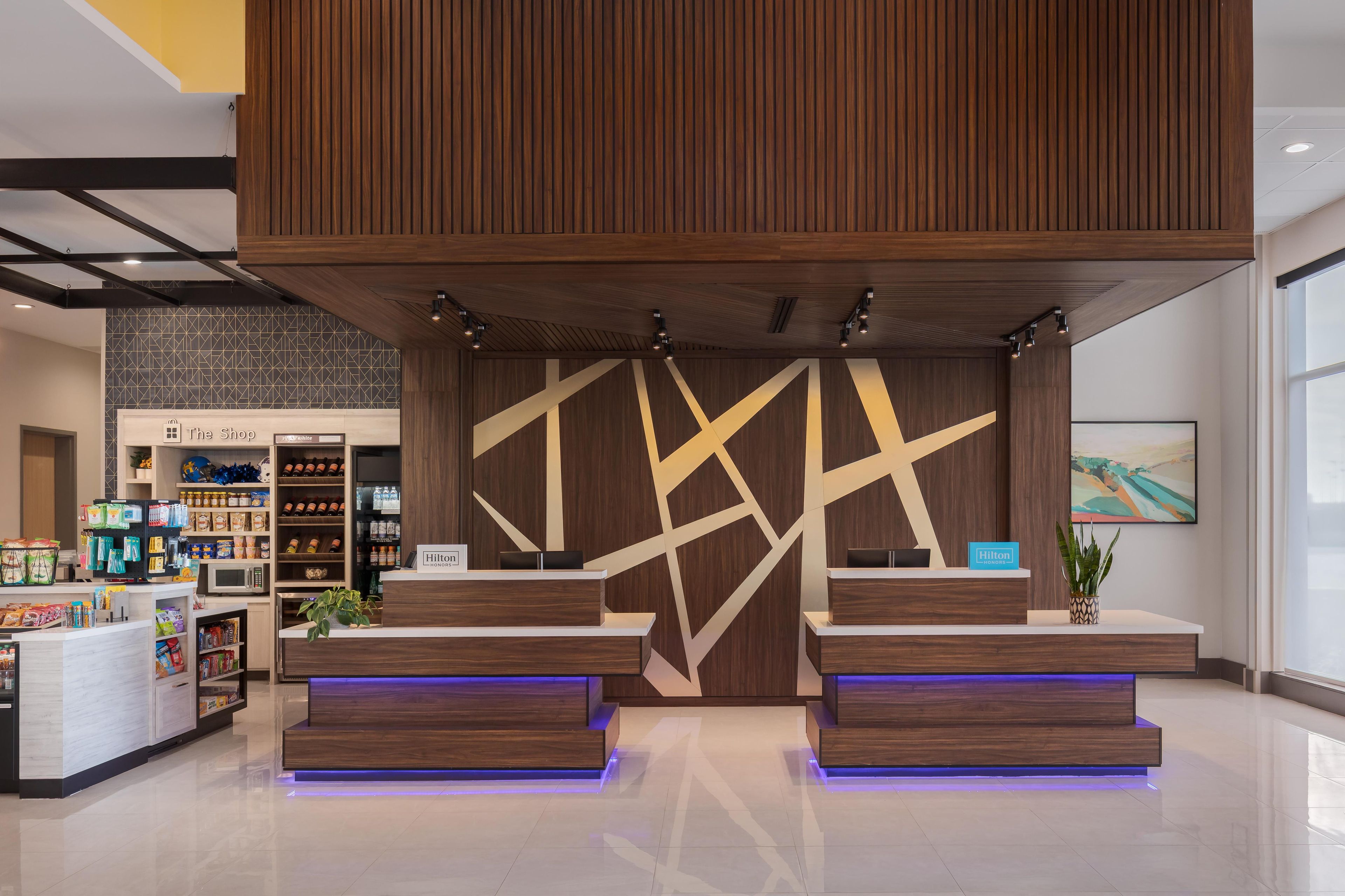 A hotel reception area with a modern design, including a reception desk, a minibar, and a view of the lobby.