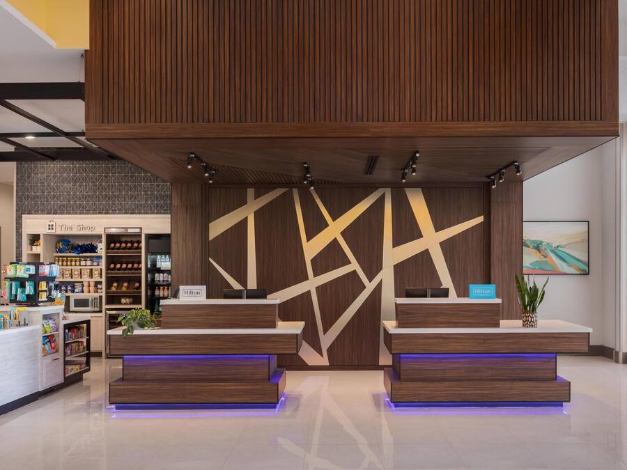 Zona de recepción de hotel con diseño moderno, que incluye un mostrador de recepción, una barra de minibar y vistas al vestíbulo.