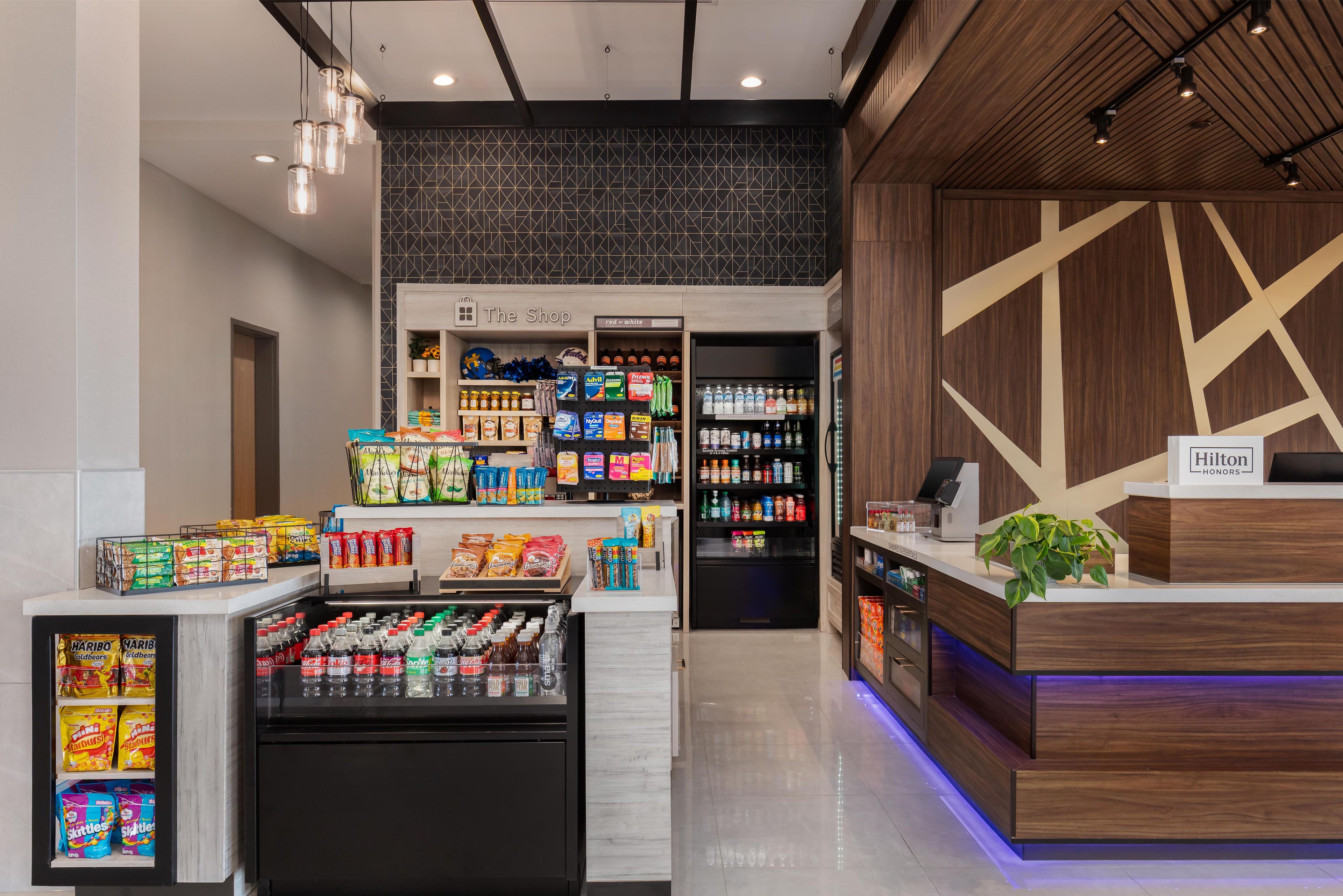 Un vestíbulo de hotel con mostrador de recepción, un minibar, exhibición de bocadillos y un refrigerador para bebidas.