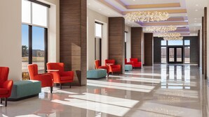 Un vestíbulo amplio con sillones modernos rojo y aguamarina, ventanas grandes y piso pulido.