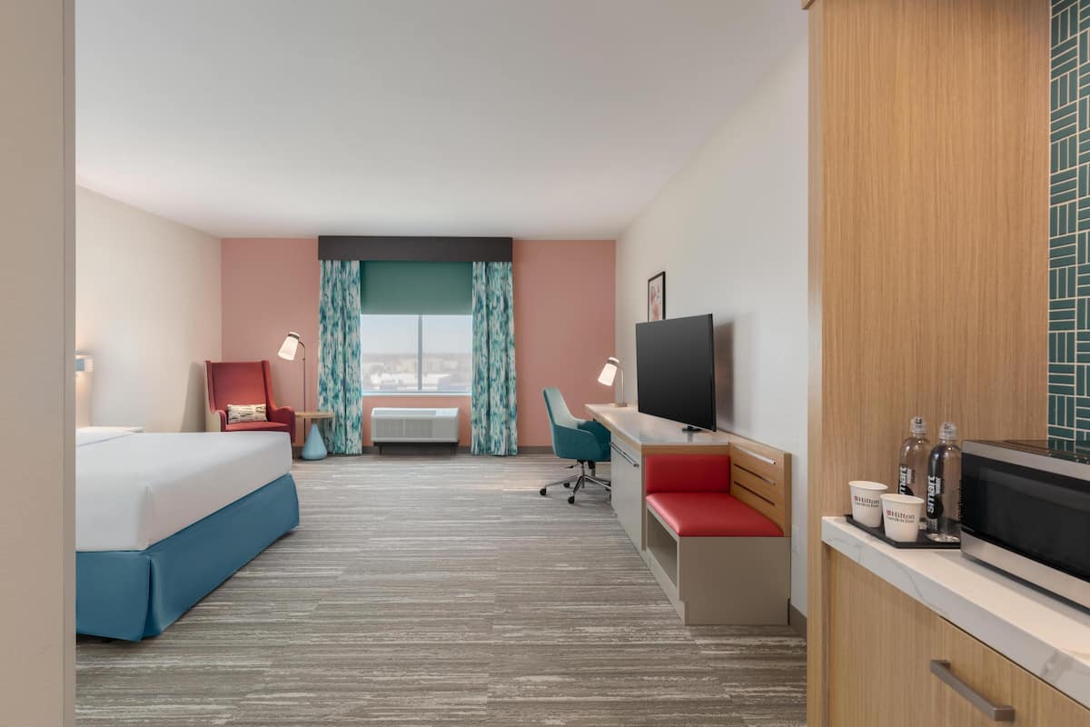 A hotel room with a bed, desk, TV, and kitchenette.
