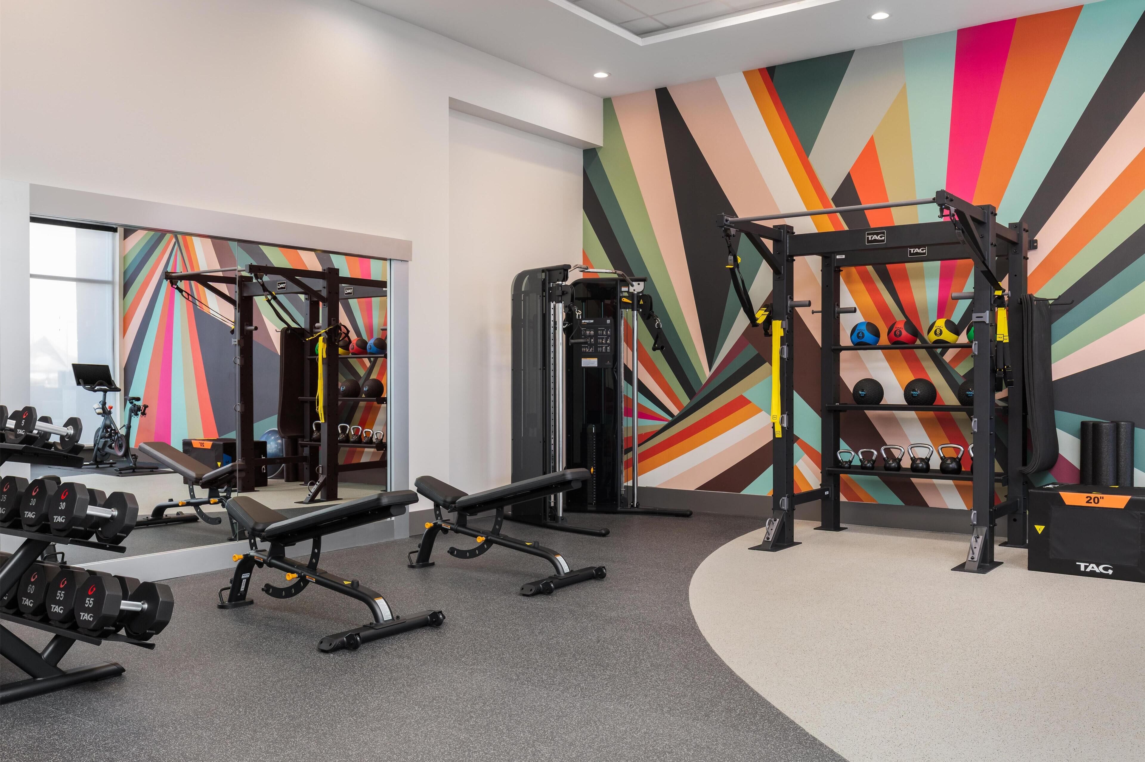 A gym with weightlifting equipment, benches, and a colorful wall mural.