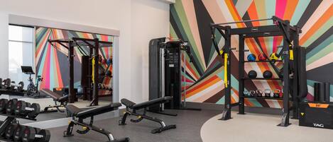 A gym with weightlifting equipment, benches, and a colorful wall mural.