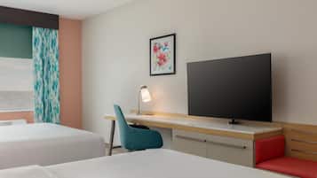 Habitación de hotel con dos camas, un escritorio, televisión, lámpara y ventana con cortinas.