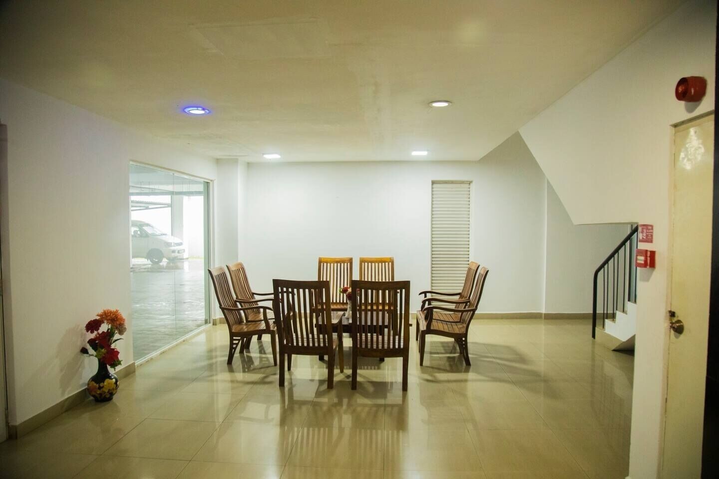 A spacious room with a dining table and chairs, a vase with flowers, and a staircase leading to another floor.