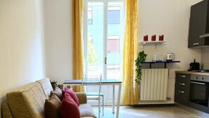 Una sala de estar con sofá, una mesa de comedor y una zona de cocina con armarios y electrodomésticos.