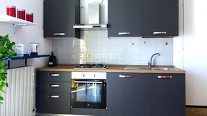 Una cocina moderna con armarios oscuros, estufa a gas, horno empotrado y pileta de acero inoxidable.