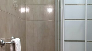 Un baño con cabina de ducha de vidrio, inodoro blanco y un pequeño estante con artículos de aseo.