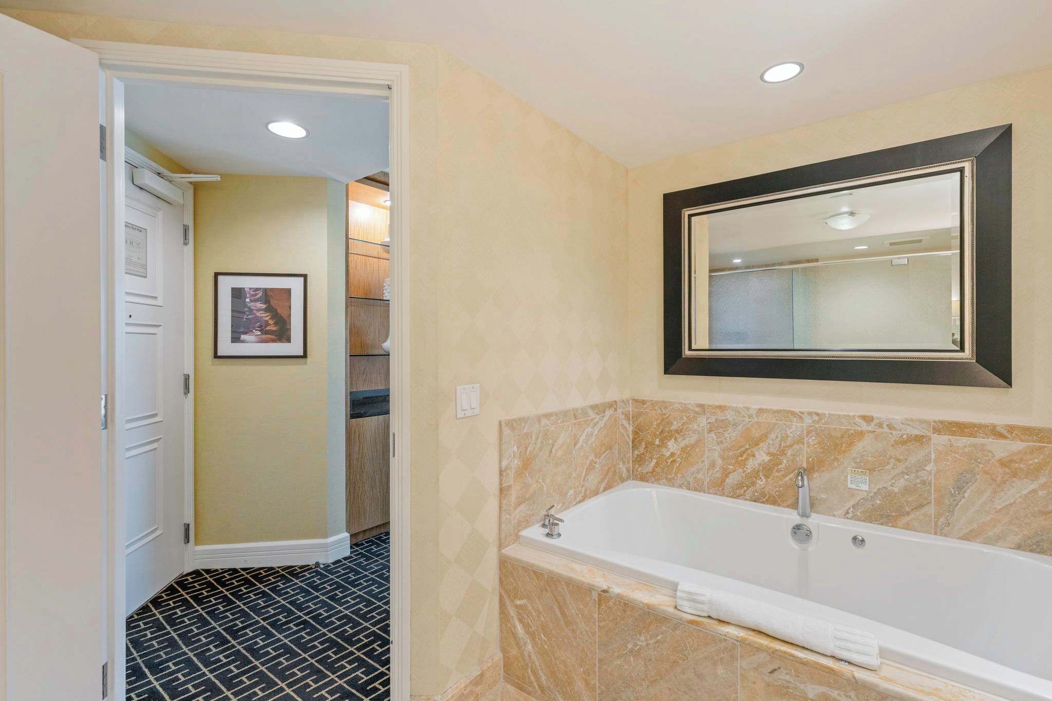 A bathroom with a marble bathtub, a framed mirror, and a black and white patterned floor.