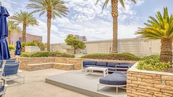 Un área de estar al aire libre con asientos, palmeras y una vista de un edificio moderno al fondo.