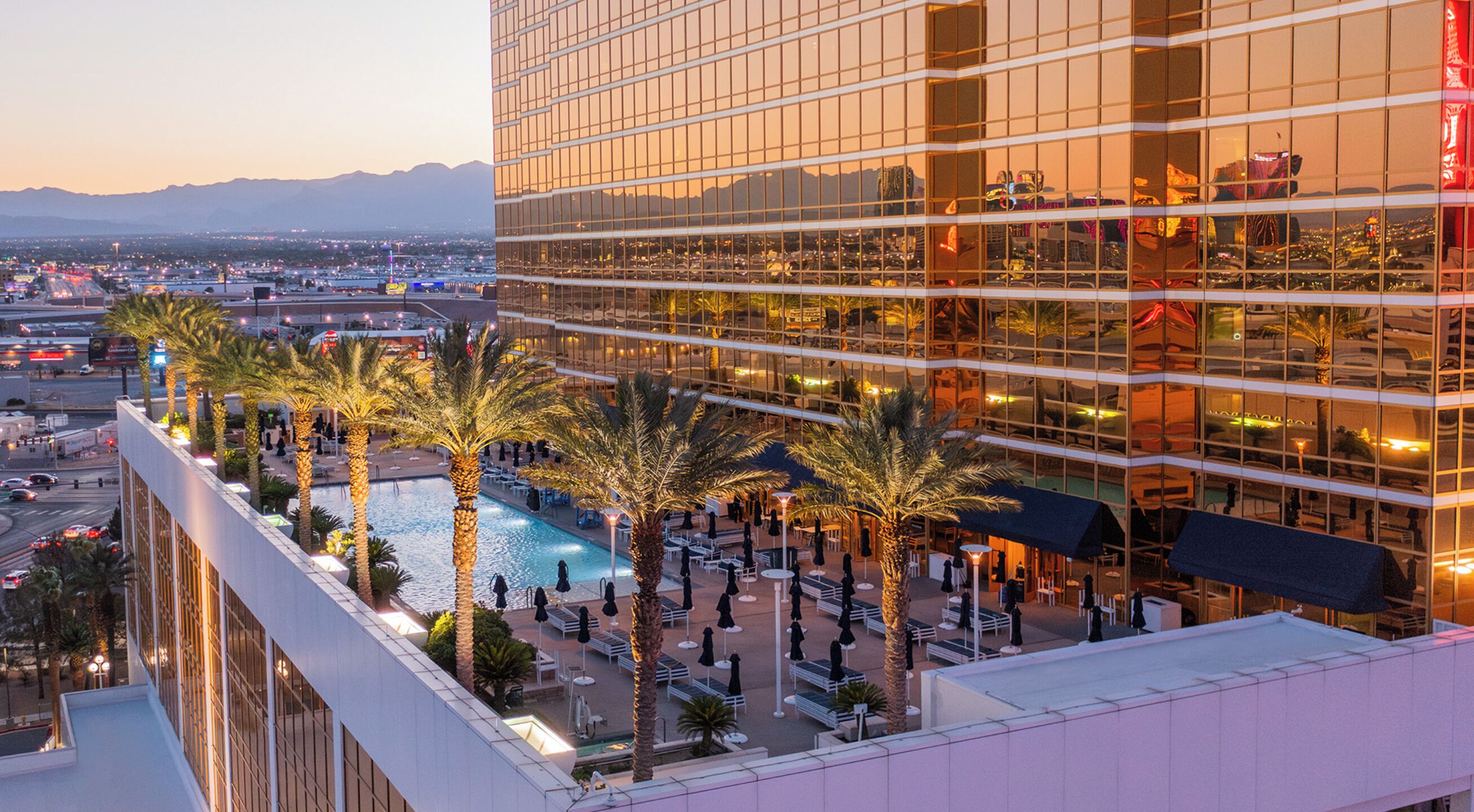 A high-rise hotel with a rooftop pool, palm trees, and a view of the cityscape.